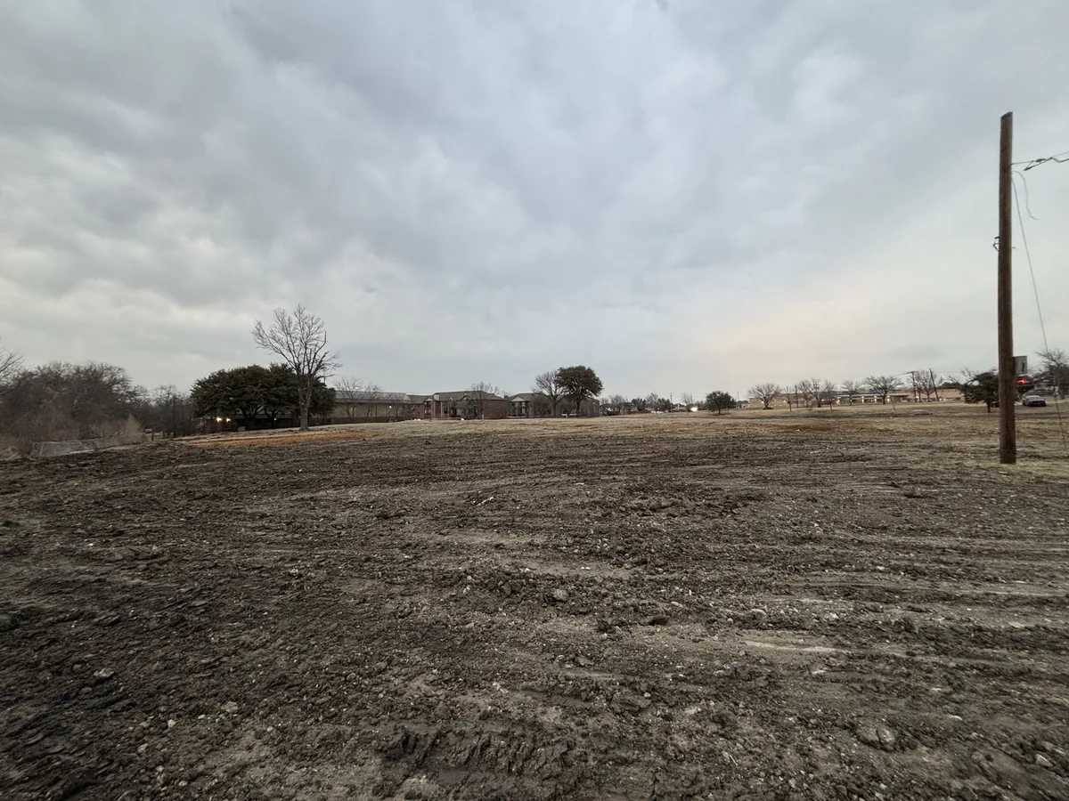 Wide cleared and graded field under an overcast sky with a utility pole at the edge