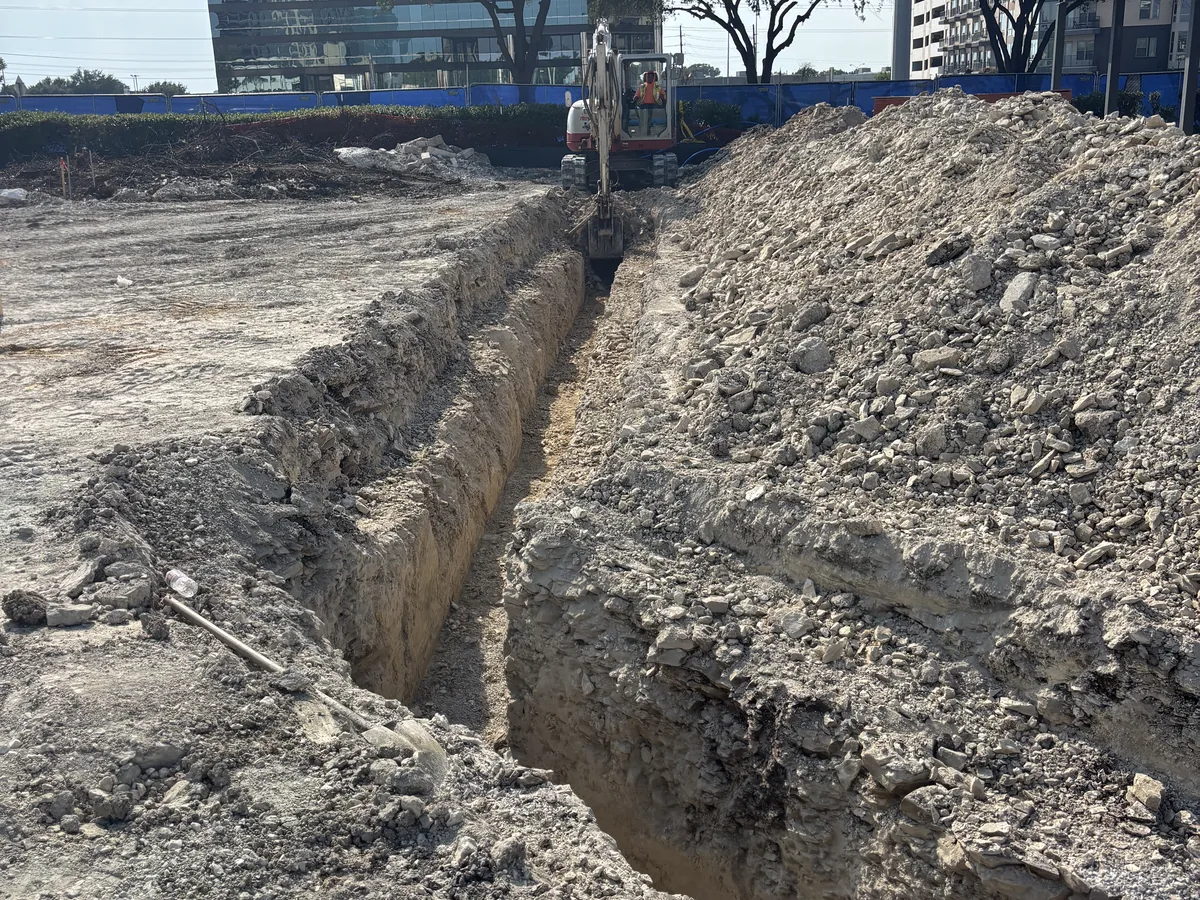 Long deep utility trench cut across a commercial site with spoil piled along both sides