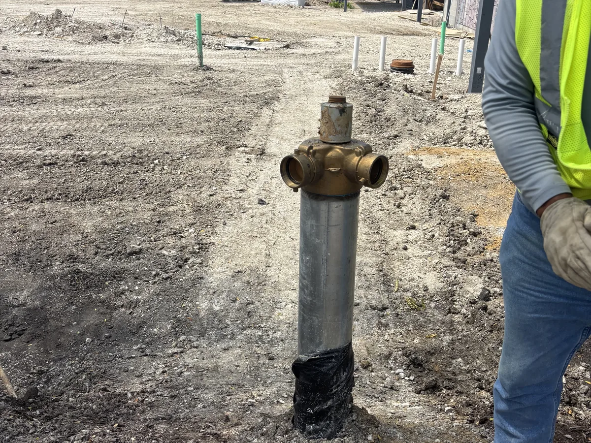 Worker steadying an upright galvanized riser pipe with a brass valve head