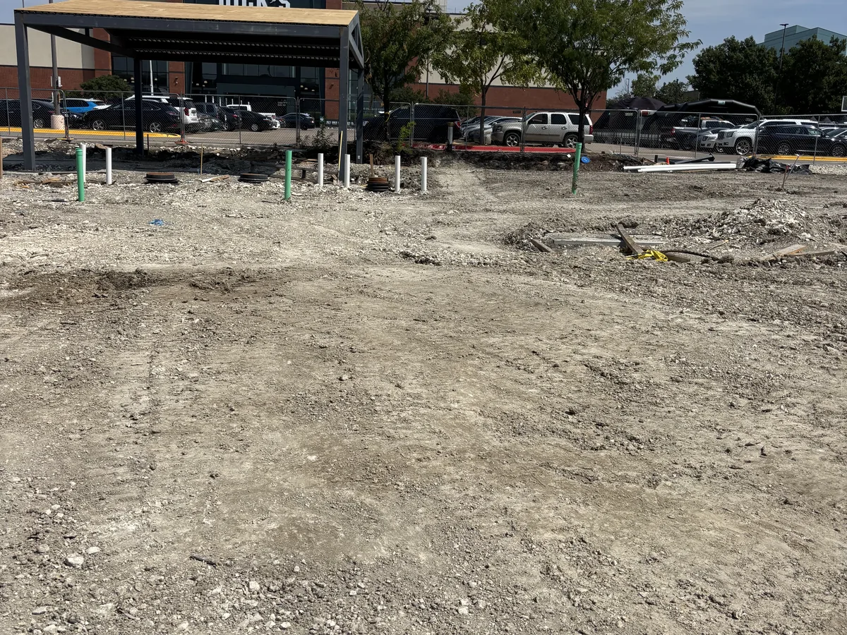 Flat graded commercial pad site with utility marker stakes set across it and a retail building behind