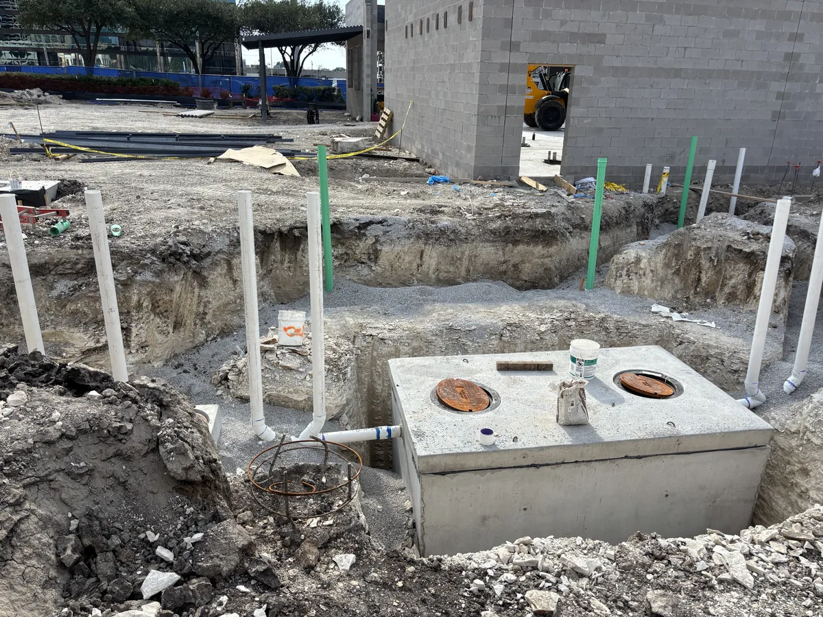 Precast concrete grease trap set in an excavation with capped pipe stubs and a block building