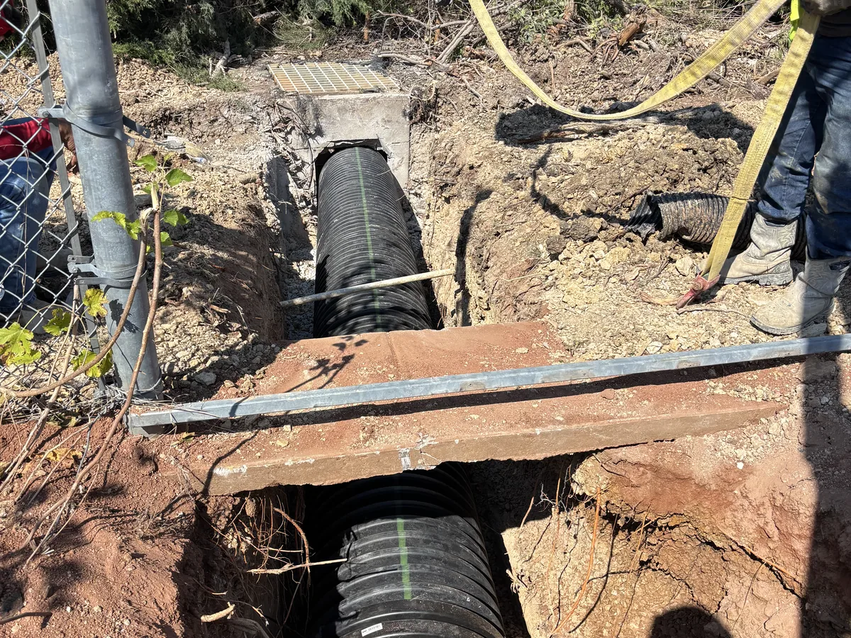 Black corrugated HDPE pipe laid in an open trench with timber shoring boards across the top