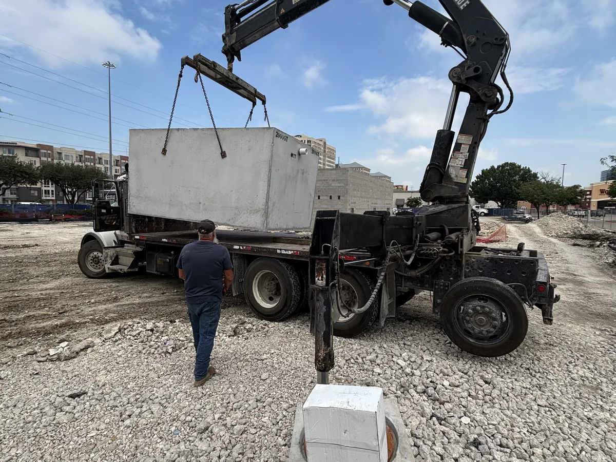 Knuckle boom crane lifting a large precast concrete vault off a flatbed truck