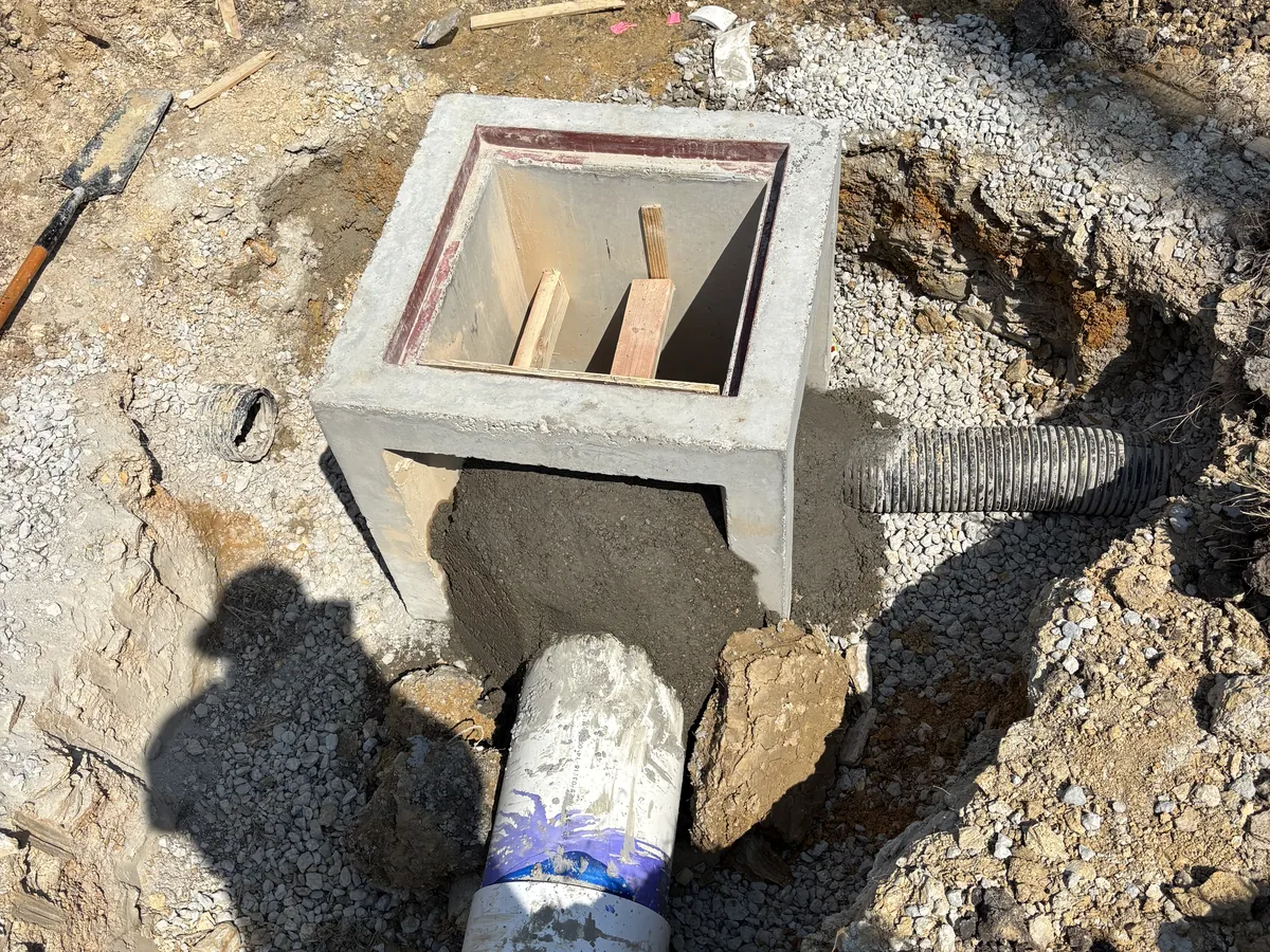 Small precast concrete junction box set in gravel with corrugated pipe connected at one side