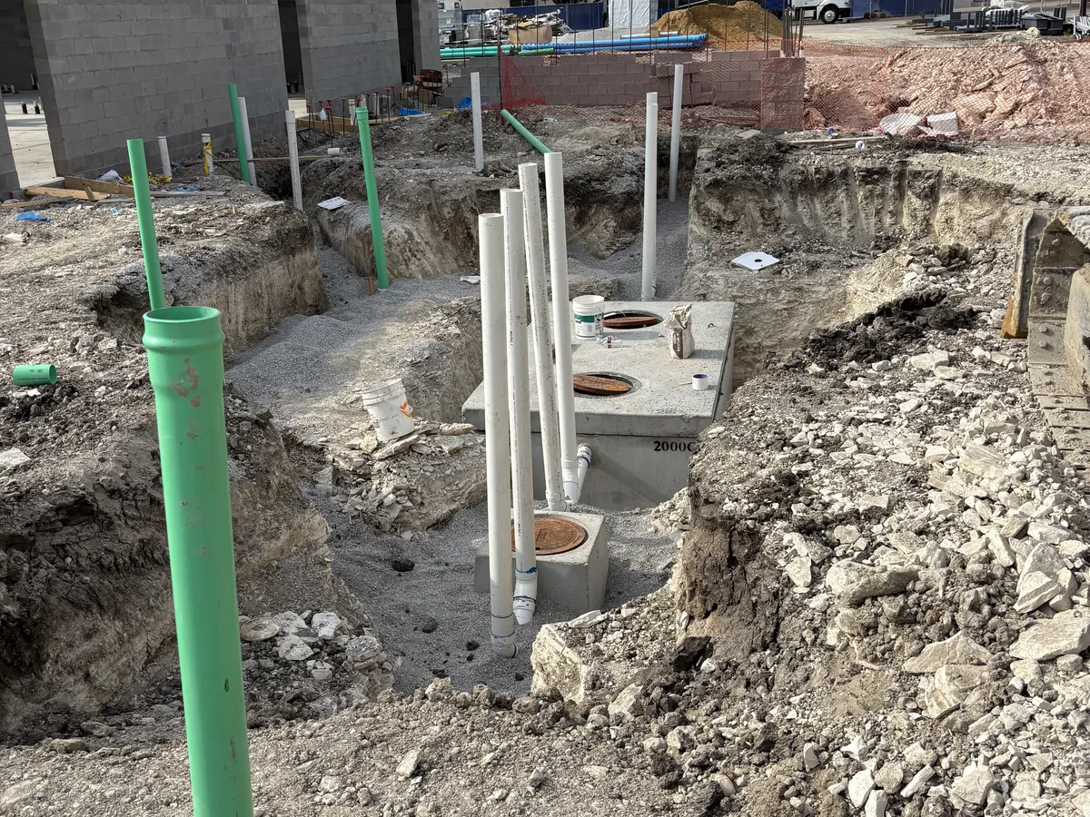 Green and white PVC pipe risers standing in an open excavation next to a set precast structure
