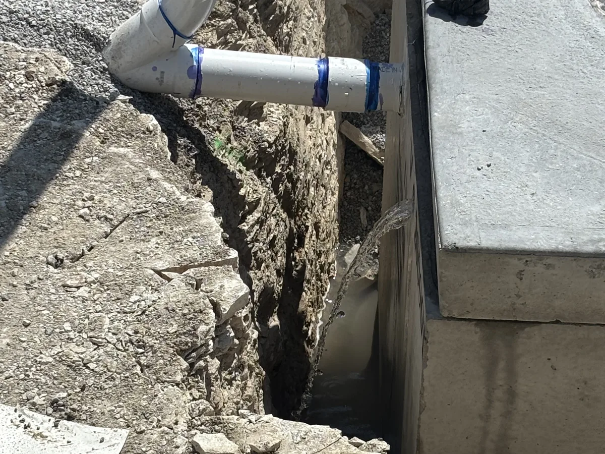 Large white PVC pipe running into a concrete drainage structure at the bottom of a sloped excavation