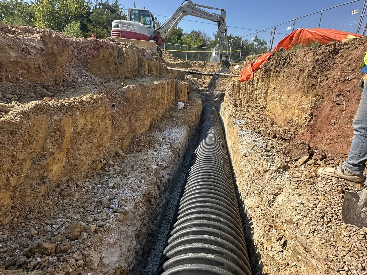 Corrugated storm sewer pipe run along an open trench with an excavator