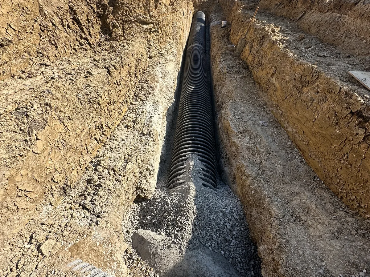 Two corrugated drain pipes running side by side down a trench in orange clay soil