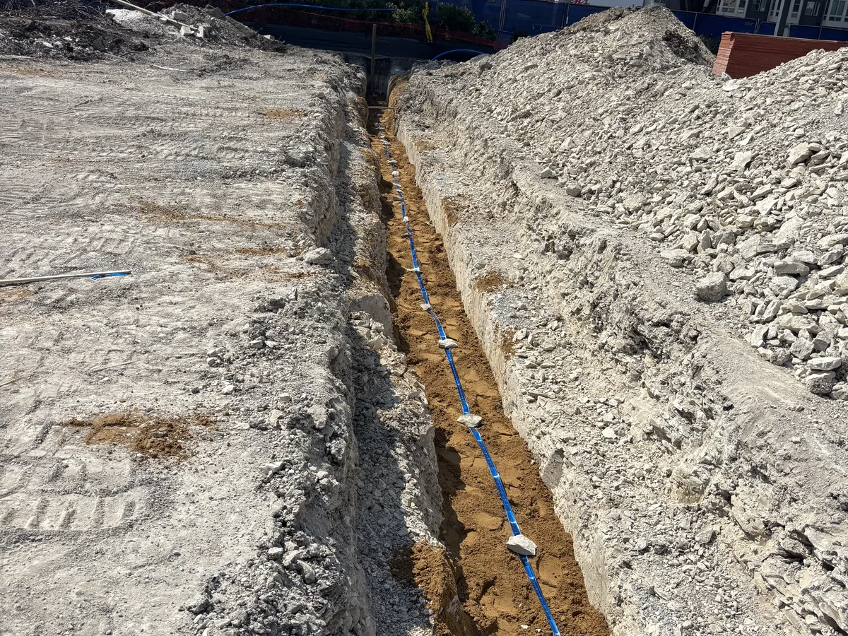 Straight trench running toward the horizon with a utility line set at the bottom and rock spoil alongside